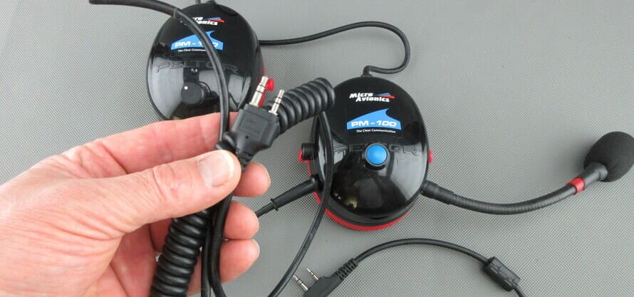 Een MicroAvionics® headset met radio-aansluitkabel, waarbij de radiostekker in een hand wordt gehouden.